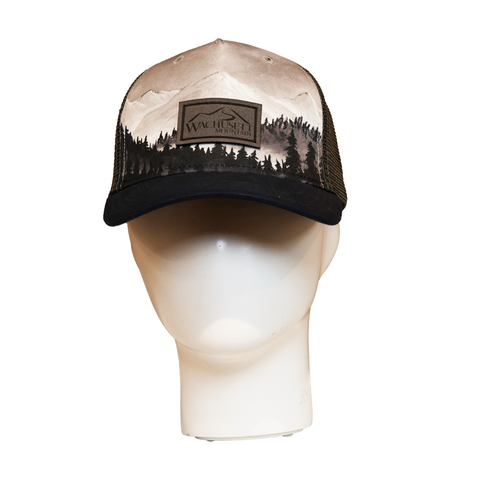 Front view of a trucker hat with a printed mountain and forest scene in earthy tones. The crown features a stitched patch reading "Wachusett Mountain," and the bill is black. Displayed on a white mannequin head.